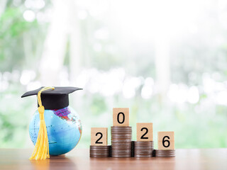 Earth globe with graduation hat, Wooden block with number 2026 on stack of coins. The concept of...