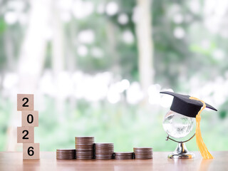 Glass earth globe with graduation hat, Wooden block with number 2026 and stack of coins. The...