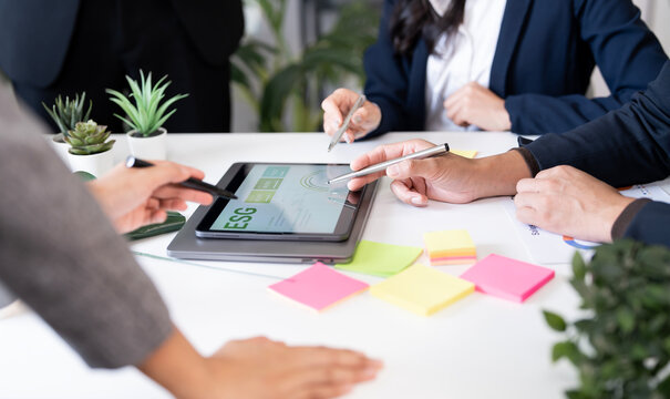 Close-up of businesspeople analyzing ESG data on tablet during meeting, discussing sustainable strategy with teamwork and collaboration in modern office environment. - Powered by Adobe