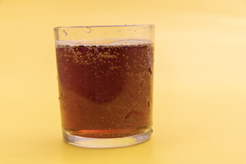 Glass of traditional fizzy kvass with bubbles on vibrant yellow background