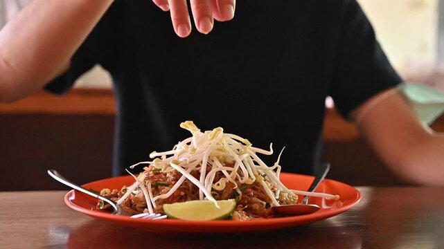 Woman adding bean sprout to her Pad Thai before eating. Pad thai represents a blend of three flavors salty, sweet, and sour which are the fundamentals of Thai cuisine.