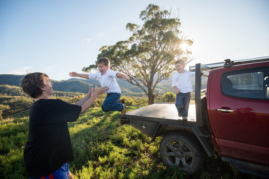 Happy kids jumping off back of ute to teenage boy in the Australian bush