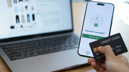 Using smartphone to confirm a payment while holding a credit card in front of a laptop, illustrating seamless device connectivity and easy digital payment
