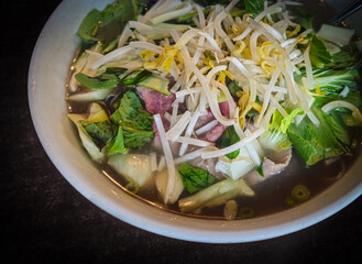 Closeup of a bowl of Pho, a traditional Vietnamese noodle soup, served with thinly sliced beef and fresh garnishes