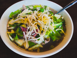 Closeup of a bowl of Pho, a traditional Vietnamese noodle soup, isolated on a table and served with fresh garnishes