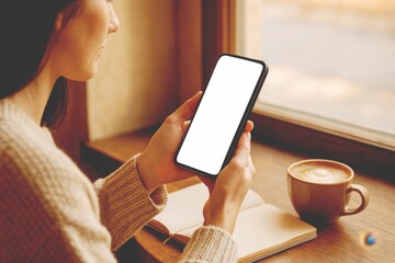 Mockup, woman's hands holding mobile phone with blank screen in coffee shop.