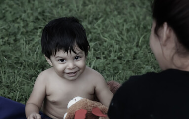 A Mexican baby smiling while a woman is near him, outside, as she looks at him