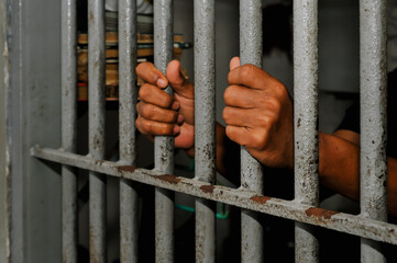 prisoner's hands behind bars with black background	