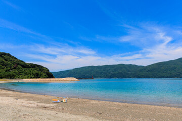 砂浜から望むムーンビーチ井野浦と防波堤、遠くに見える風車の夏景色

