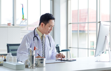 Asian male doctor in white coat with stethoscope, consulting digital tablet for health reading in modern hospital medical clinic office, research professional healthcare insurance wellness technology.