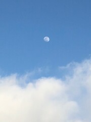Moon during day. Blue sky with clouds.
