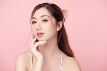 A beautiful young Asian woman with clean, fresh skin against a pink background. Skincare, facial treatment, cosmetology, beauty, and spa. An elegant portrait of an Asian woman.