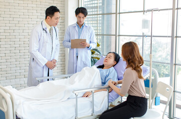 Obraz premium Asian man doctor and medical team visiting ward, consulting, talking to physician, senior woman patient lying on hospital bed room explaining medical treatment with family member showing care support.