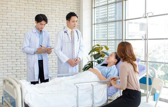 Asian man doctor and medical team visiting ward, consulting, talking to physician, senior woman patient lying on hospital bed room explaining medical treatment with family member showing care support