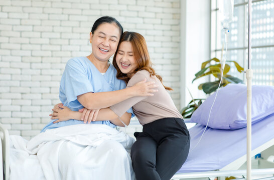 Asian happy family emotional support smiling elderly senior woman mother patient sitting hugging with lovely daughter cheering on hospital bed showing take care healthcare insurance treatment wellness