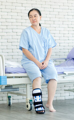 Asian middle-aged female senior woman patient resting sitting on bed at hospital wearing splint leg support ankle foot orthosis, calm but tired thoughtful looking away, healthcare wellness insurance.