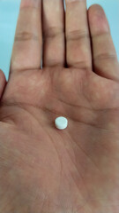 Single white round pill on human palm, close-up photo representing medication, pharmaceutical drug, or health supplement concept
