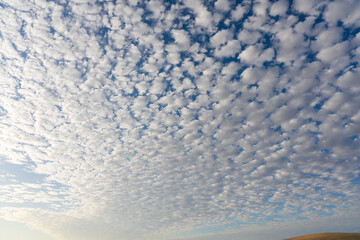 An expansive blue sky is filled with a textured pattern of scattered, puffy white clouds, creating...