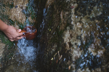 A peaceful moment of someone gathering water with a wooden cup from a clear natural stream, highlighting simplicity and the harmony of nature.