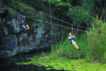 An adventurous couple riding a zipline over a jungle lake in a tropical destination. Smiling and having a thrilling, fun time while on vacation