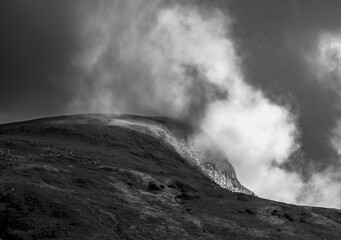 Low cloud drifting over mountain ridge in moody monochrome landscape