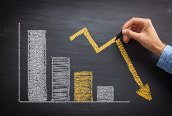 Hand drawing a downward trending bar graph and arrow on a chalkboard, symbolizing financial loss and economic decline