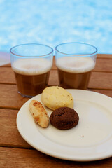 Glasses of iced coffee and cookies near the pool on blurred nature background. Vacation, resort, summer, travel concept.
