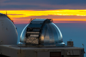 Astronomical observatories atop Mauna Kea, Hawaii, stand above the clouds at sunset, capturing a...