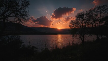 Obraz premium Serene Sunset Over a Calm Lake with Silhouetted Trees and Hills