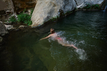 Obraz premium A young woman enjoys a peaceful and serene swim in a natural stream surrounded by rocks and lush greenery, showcasing a moment of relaxation in nature.