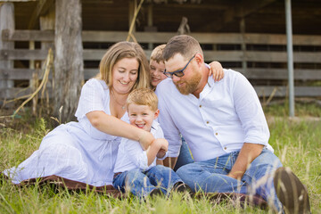 Family portrait sitting together on grass in front of shearing shed on farm