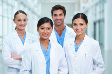 Fototapeta premium Diverse team of smiling medical professionals in white lab coats standing in a modern hospital hallway
