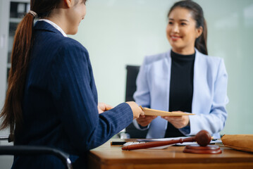 Two professional women shake hands over a signed contract at a legal office desk, symbolizing...