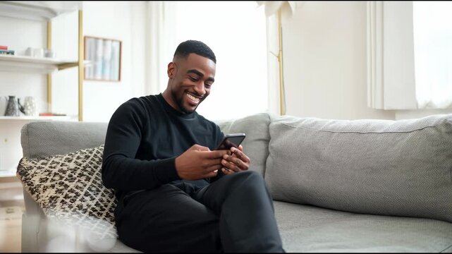 Young man smiling while using smartphone on comfortable couch