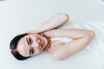 Beautiful woman in wedding dress lying on white bed