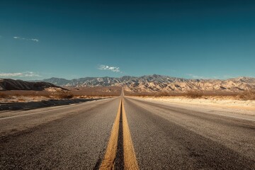 Naklejka premium Long stretch of endless road cutting through a barren desert landscape with mountains in the distance under a clear blue sky