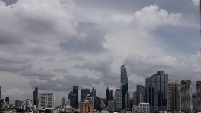 Time-lapse of fluffy white cumulus clouds drifting above the city skyscrapers on a clear blue sky day