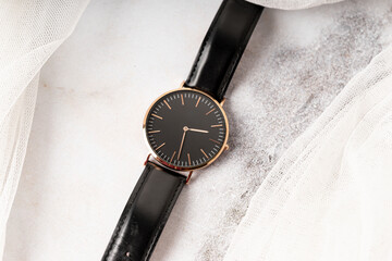 minimalist black wristwatch with a gold rim and leather strap, displayed on a marble surface, with...