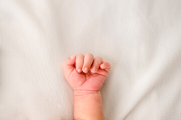 Close-up of a newborn baby hand gently curled on a soft white blanket, symbolizing innocence and...