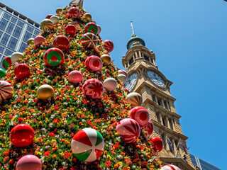 Giant Christmas tree decorated with colorful ornaments and flowers standing in Sydney near clock...