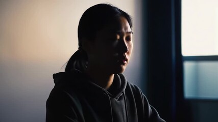 Dark portrait of a woman with light surrounding her face, looking downward. Ideal for book covers, magazines, or blog posts.