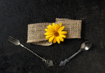Artistic arrangement of vintage cutlery with floral accent and textured ribbon