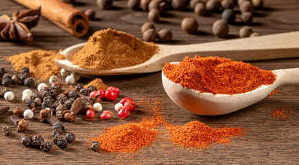 Two wooden spoons holding bright spices and scattered peppercorns on a rustic table