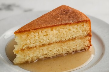 A delicious slice of golden sponge cake drizzled with syrup on a white plate