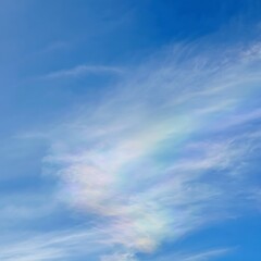 Fototapeta premium Iridescent clouds display shimmering pastel colors against a bright, clear blue daytime sky