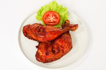 Two juicy, brown grilled chicken legs, glistening with a rich sauce and served on a white plate. Captured with natural light on a white background.