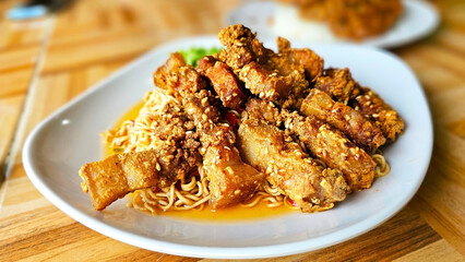 Instant noodle spicy salad with crispy pork belly : A mouthwatering close-up shot of succulent, golden-brown fried pork belly served atop a bed of perfectly cooked noodles. Yum mama