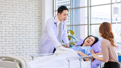 Asian man professional doctor visiting ward, consulting talking to physician, senior woman patient lying on hospital bed experiencing pain symptoms with her lovely daughter family showing care support