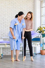 Fototapeta premium Asian young woman teaching walking support crutches walks beside senior female patient in hospital bed room medical recovery caregiver specialist wellness healthcare treatment rehabilitation support.