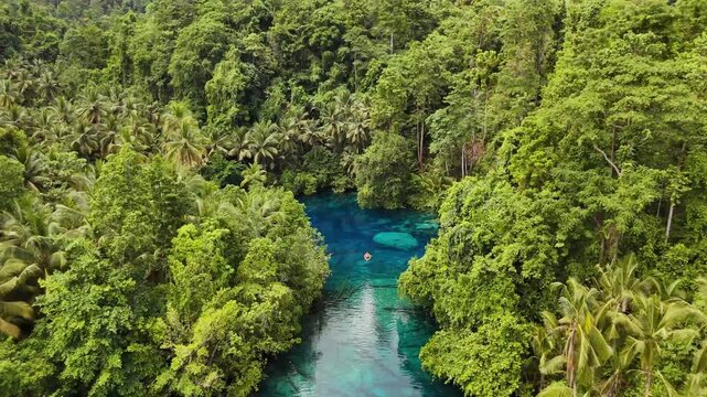 4k drone video flying towards a small rowing boat at Paisupok Lake, Banggai Islands, Sulawesi Indonesia. The clearest lake in the world is surrounded by tropical jungle landscapes.